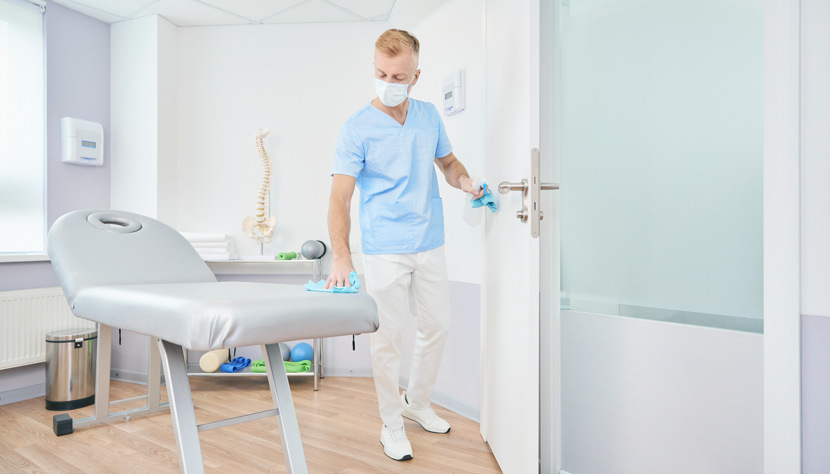 Mitarbeiterin reinigt eine Behandlungsliege und Kontaktfläche in einer Praxis als Beispiel für ambulante Hygiene