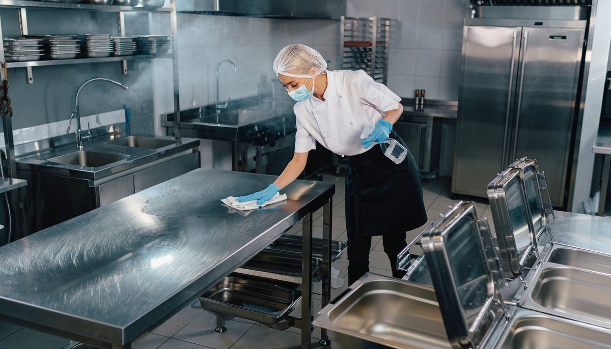 Mitarbeiter reinigt Edelstahlflächen und Buffetkomponenten in einer Cateringküche nach dem Service