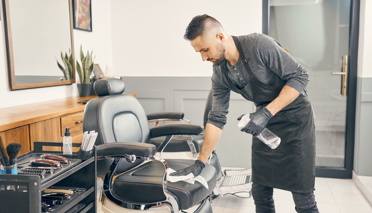 Friseur reinigt Armlehnen, Ablage und Türgriff in einem Barbershop zwischen Kundenterminen