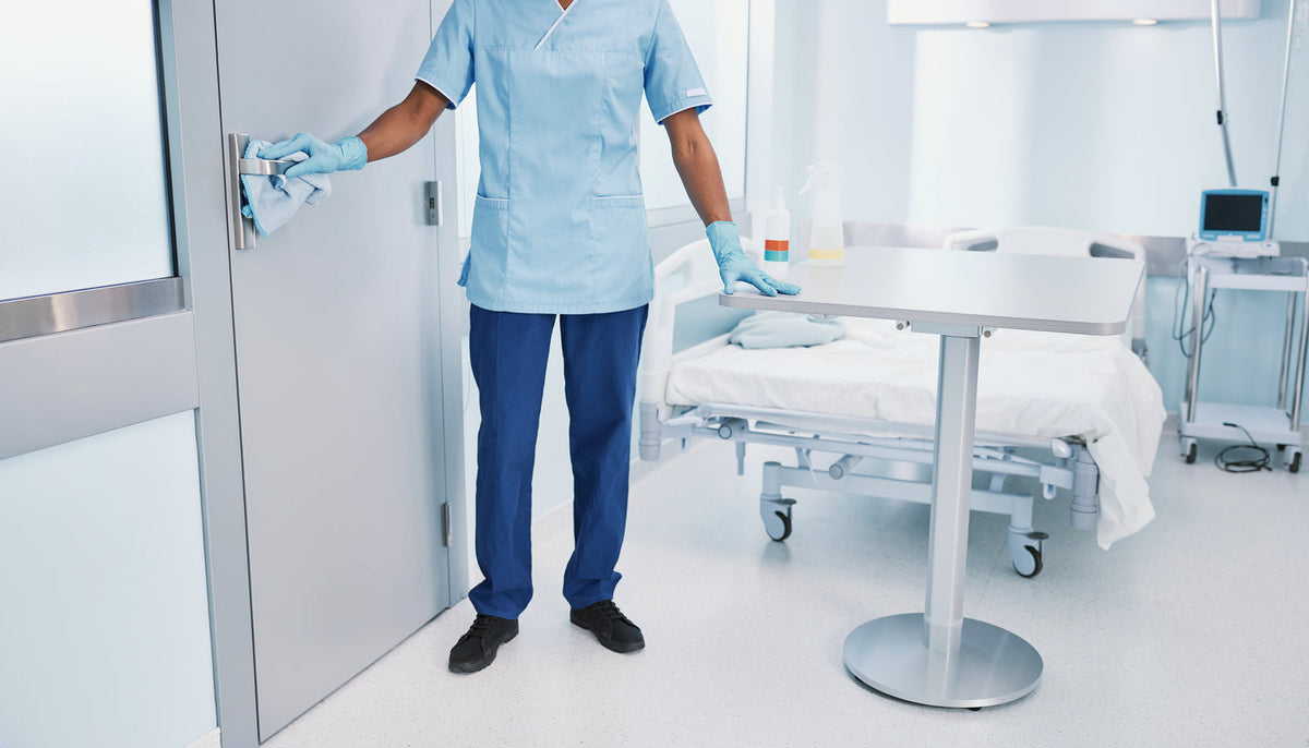 Reinigungskraft reinigt Kontaktflächen in einem Patientenzimmer als Beispiel für Umgebungshygiene bei MRSA und MRE