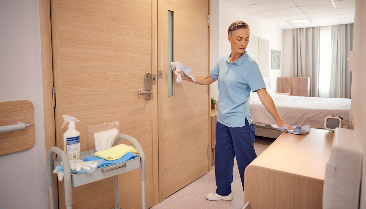 Pflegekraft reinigt Kontaktflächen in einem Pflegezimmer als Beispiel für verstärkte Hygiene bei Norovirus