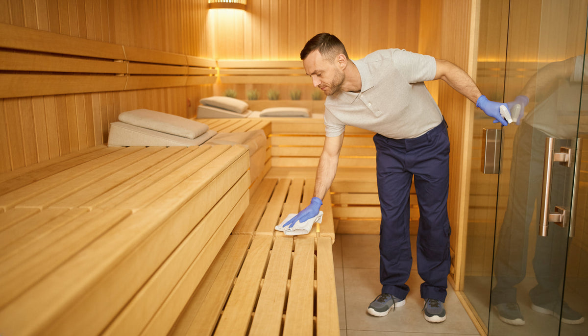 Reinigungskraft reinigt eine Saunabank und Kontaktflächen in einem modernen Wellnessbereich
