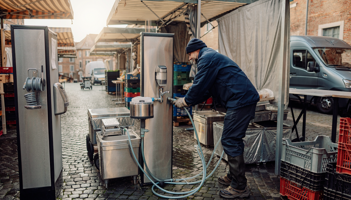 Marktbeschicker schließt eine mobile Trinkwasserstation mit lebensmittelgeeignetem Schlauch auf einem Wochenmarkt an