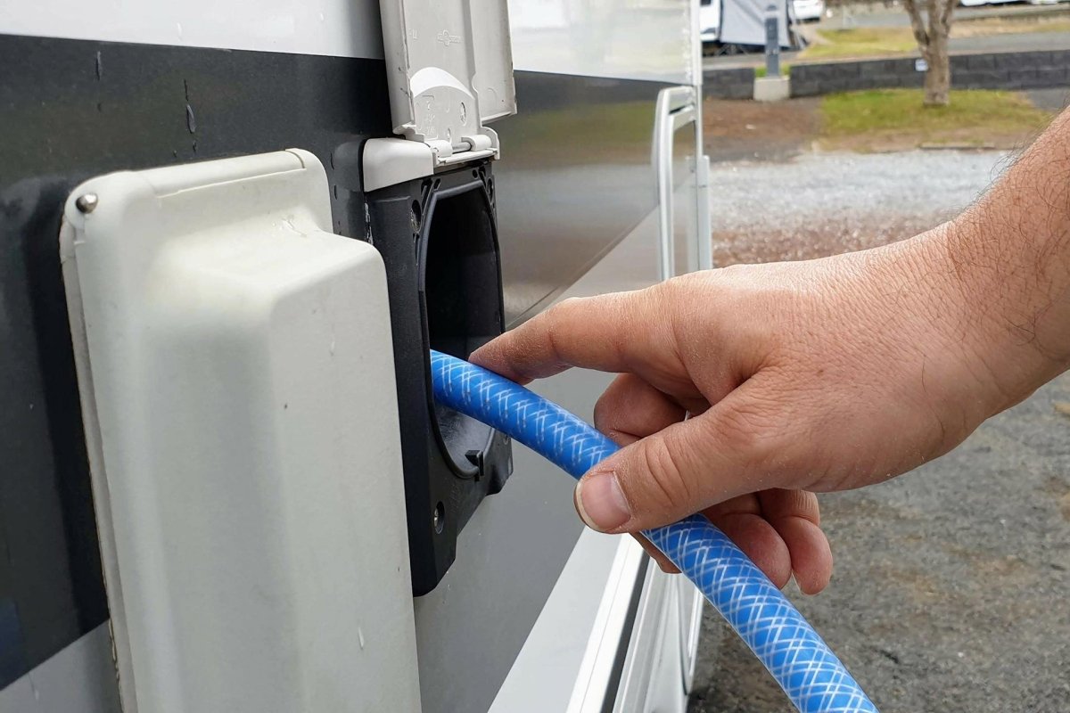Ein Mann befüllt sein Wohnmobil mit einem blauen Schlauch