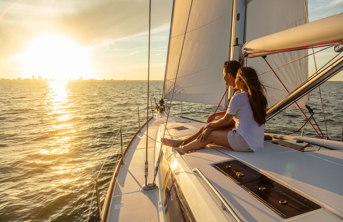 Ein Paar sitzt an Deck einer Segelyacht und sieht sich den Sonnenuntergang an